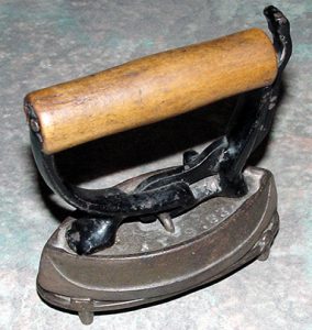 A colour photo of a 19th Century miniature sad iron for ironing lace made with cast iron base and wood handle, metal trivet (PPF Collections, Gift of Constance Snelgrove)