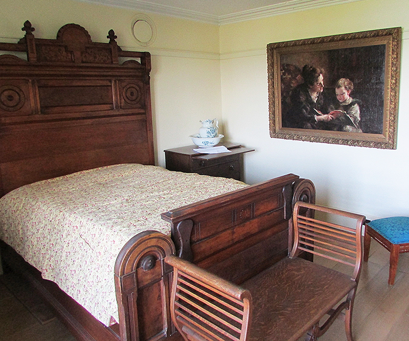 A colour photo of the front bedroom in the central wing of Horaceville showing artist John Charles Pinhey's 1894 oil portrait known as "The Picture Book", of his wife Amalia reading a story to their daughter Constance (B.E.)