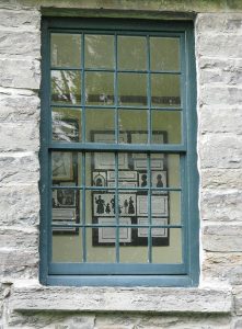 A colour photo of the window into the second floor "privy" of Horacevlle showing exhibit panels for PPF's Profiles in the Past" silhouettes exhibit (B.E.)